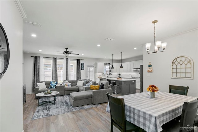 dining space featuring light hardwood / wood-style flooring, ceiling fan with notable chandelier, and ornamental molding