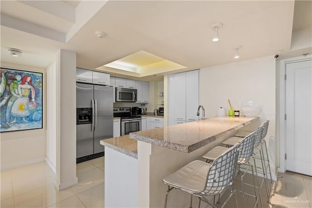 6300 Padre Blvd Unit 901, South Padre Island, TX 78597 - kitchen with stainless steel appliances, a raised ceiling, a peninsula, a kitchen breakfast bar, and white cabinetry