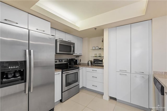 6300 Padre Blvd Unit 901, South Padre Island, TX 78597 - kitchen featuring stainless steel appliances, white cabinets, a raised ceiling, light tile patterned floors, and light stone countertops