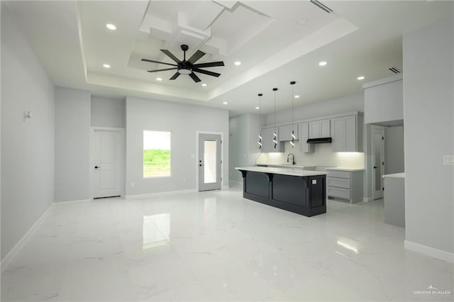 kitchen with a tray ceiling, ceiling fan, hanging light fixtures, and a spacious island