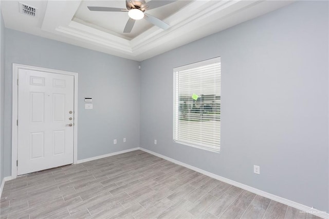 spare room featuring ceiling fan, light wood-type flooring, and a tray ceiling