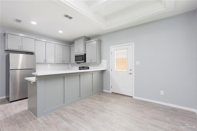 kitchen with kitchen peninsula, appliances with stainless steel finishes, light wood-type flooring, and gray cabinetry