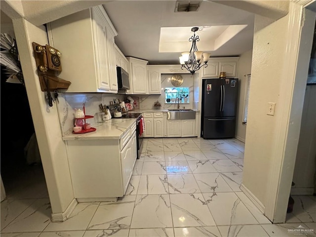 kitchen with electric range, hanging light fixtures, a raised ceiling, black fridge, and white cabinets