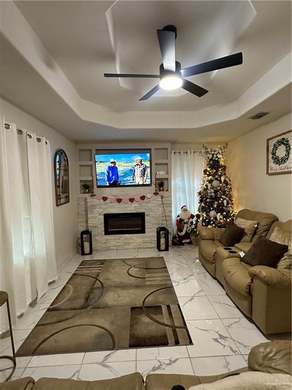 living room with ceiling fan, a raised ceiling, and built in shelves