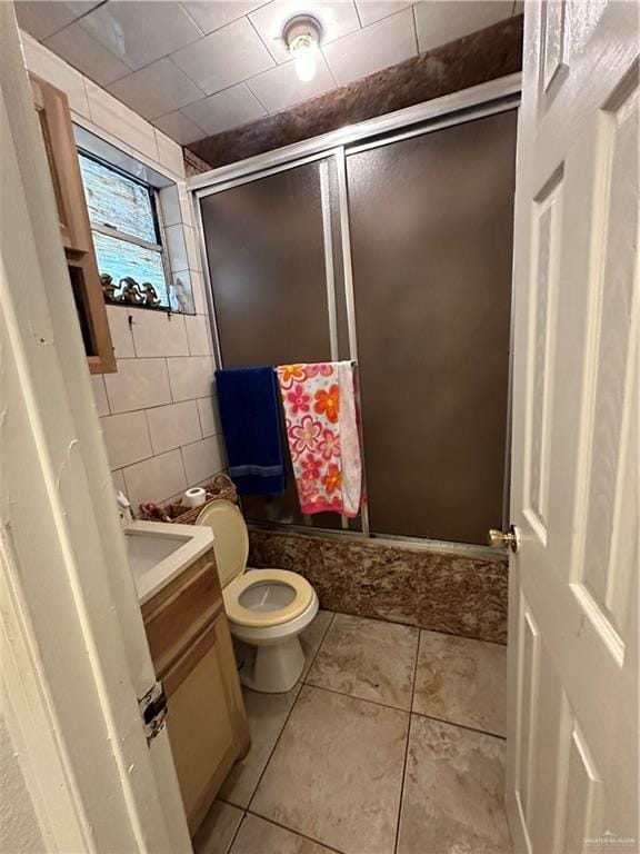 bathroom featuring tile patterned floors, toilet, a shower with door, vanity, and tile walls