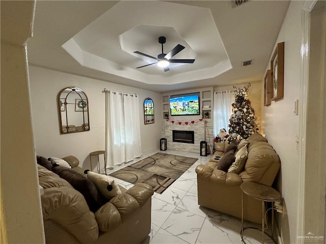 living room featuring a fireplace, a tray ceiling, and ceiling fan