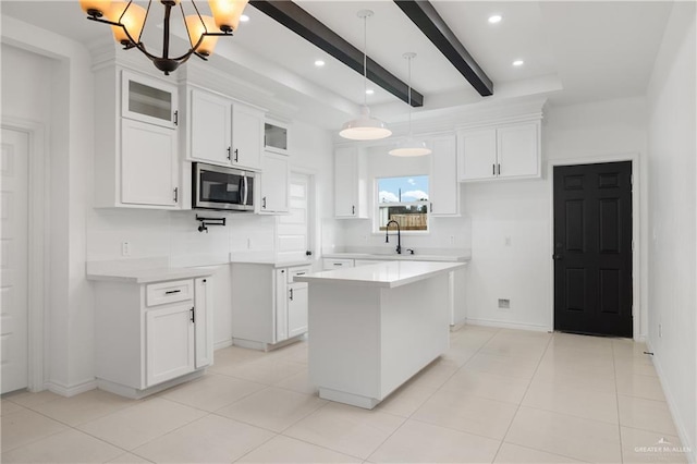 kitchen featuring sink, hanging light fixtures, beamed ceiling, a kitchen island, and white cabinetry