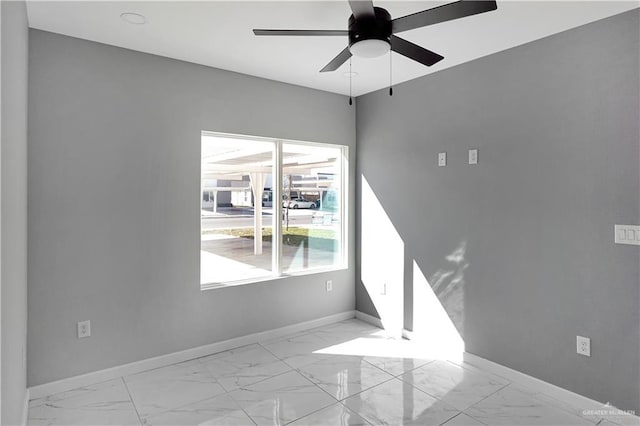 unfurnished room with a ceiling fan, marble finish floor, and baseboards