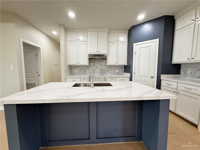 kitchen featuring white cabinetry, sink, light stone countertops, and an island with sink