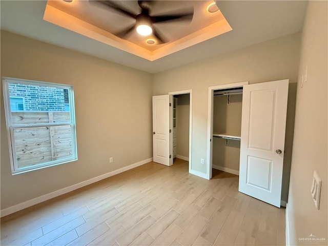 unfurnished bedroom featuring light hardwood / wood-style floors, a raised ceiling, and ceiling fan