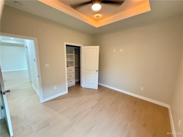 unfurnished bedroom featuring light hardwood / wood-style flooring, ceiling fan, a tray ceiling, a spacious closet, and a closet