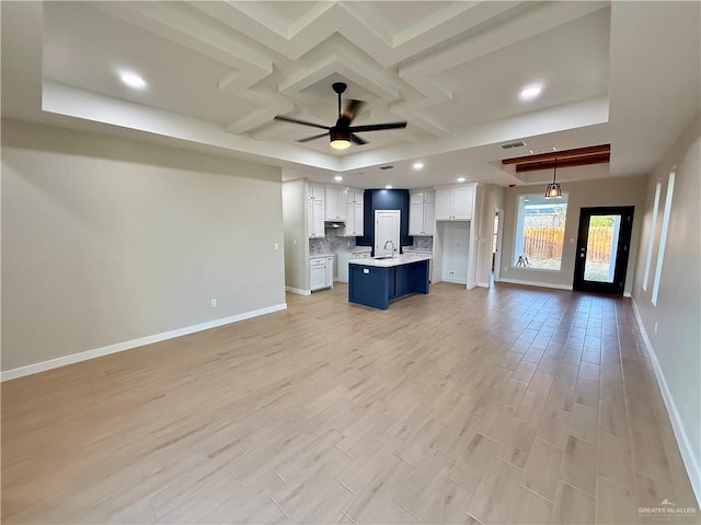 unfurnished living room featuring ceiling fan, a tray ceiling, coffered ceiling, and light hardwood / wood-style floors