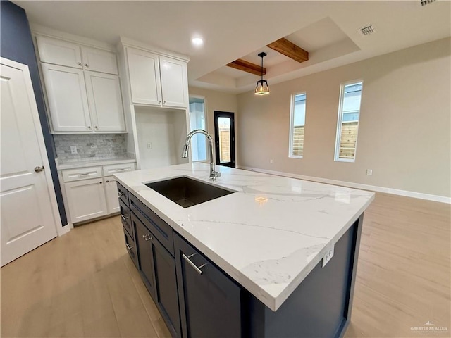 kitchen with sink, white cabinetry, a center island with sink, pendant lighting, and decorative backsplash