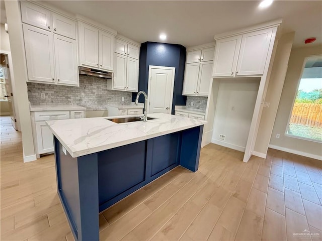 kitchen featuring an island with sink, sink, and white cabinets