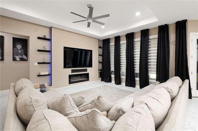 living room featuring recessed lighting, marble finish floor, a raised ceiling, a glass covered fireplace, and ceiling fan