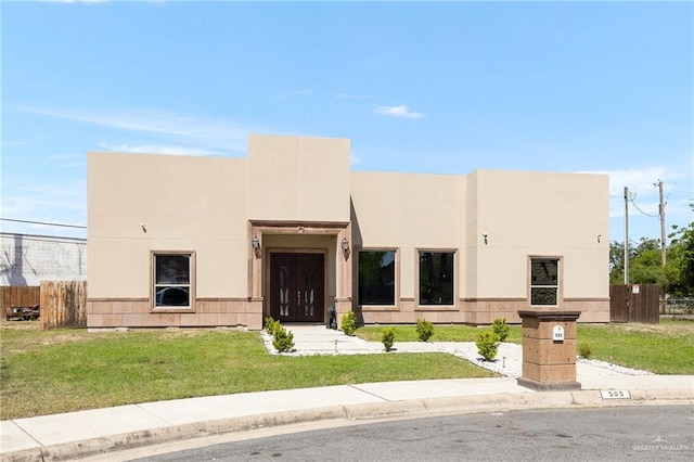 modern home with stucco siding, a front lawn, and fence