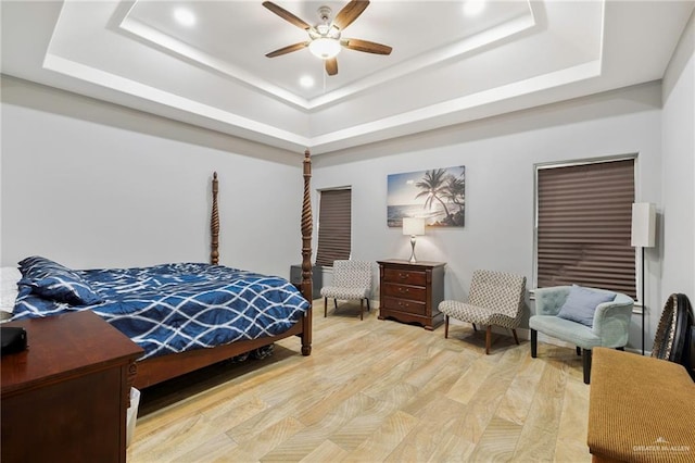 bedroom with light hardwood / wood-style floors, a raised ceiling, and ceiling fan