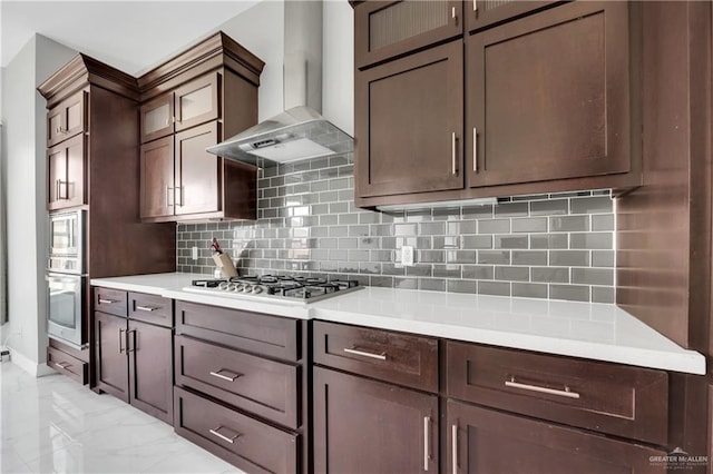 kitchen with wall chimney exhaust hood, dark brown cabinetry, decorative backsplash, and appliances with stainless steel finishes