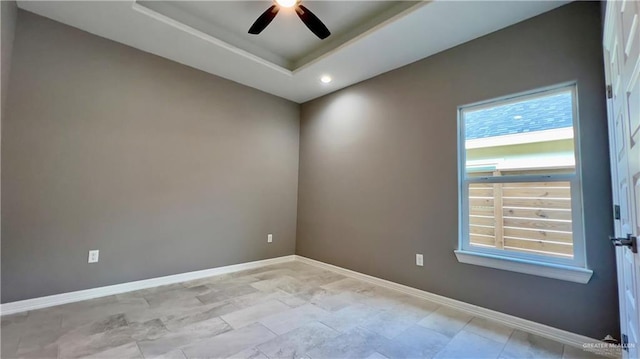 spare room with a raised ceiling, a ceiling fan, and baseboards