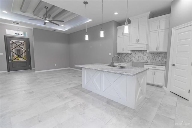 kitchen featuring a sink, white cabinets, hanging light fixtures, light stone countertops, and a raised ceiling