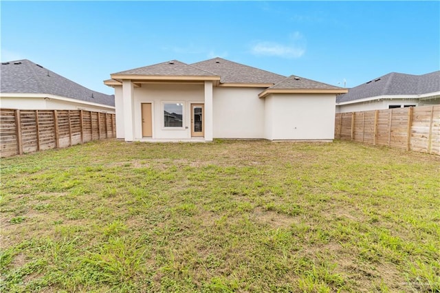 rear view of house featuring a lawn, a fenced backyard, and stucco siding