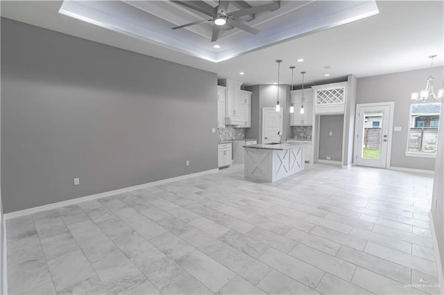 unfurnished living room featuring ceiling fan with notable chandelier, recessed lighting, a raised ceiling, and baseboards