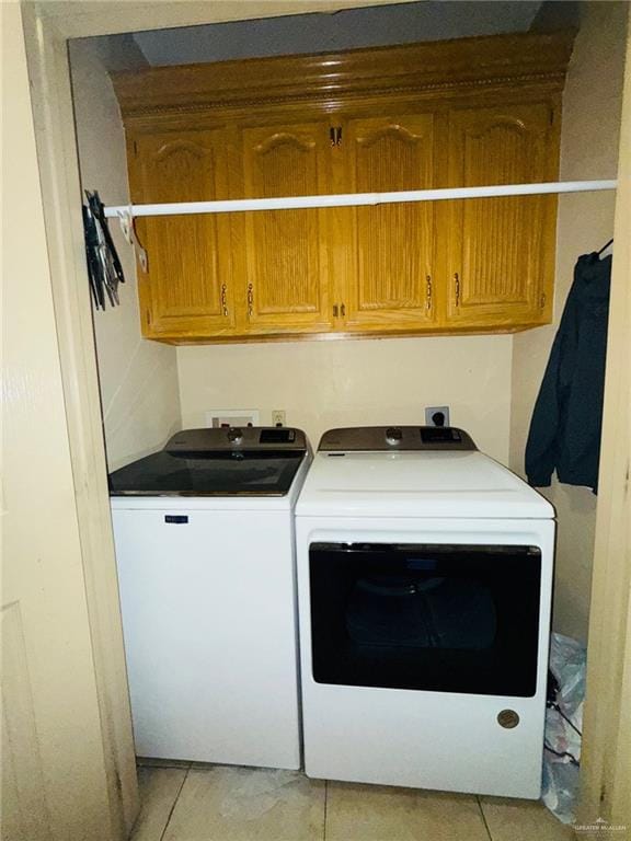 clothes washing area featuring independent washer and dryer, light tile patterned floors, and cabinets