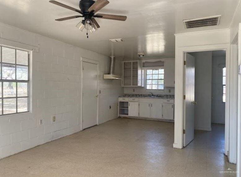 kitchen featuring ceiling fan, white cabinets, wall chimney exhaust hood, and sink