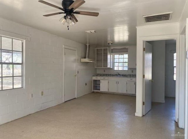 kitchen featuring ceiling fan, white cabinets, wall chimney exhaust hood, and sink