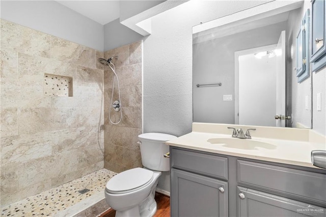 bathroom featuring hardwood / wood-style floors, vanity, a tile shower, and toilet