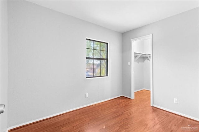 unfurnished bedroom with a spacious closet, wood-type flooring, and a closet