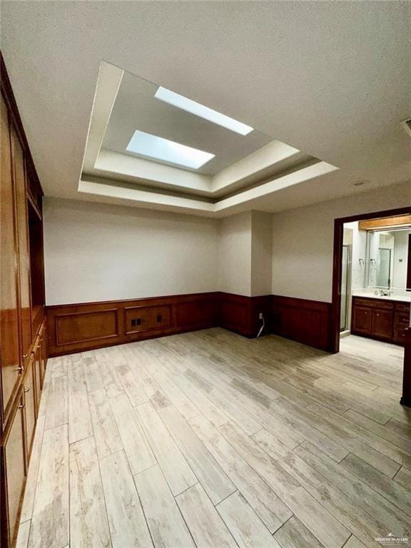 bonus room featuring a skylight, sink, light hardwood / wood-style flooring, wood walls, and a textured ceiling