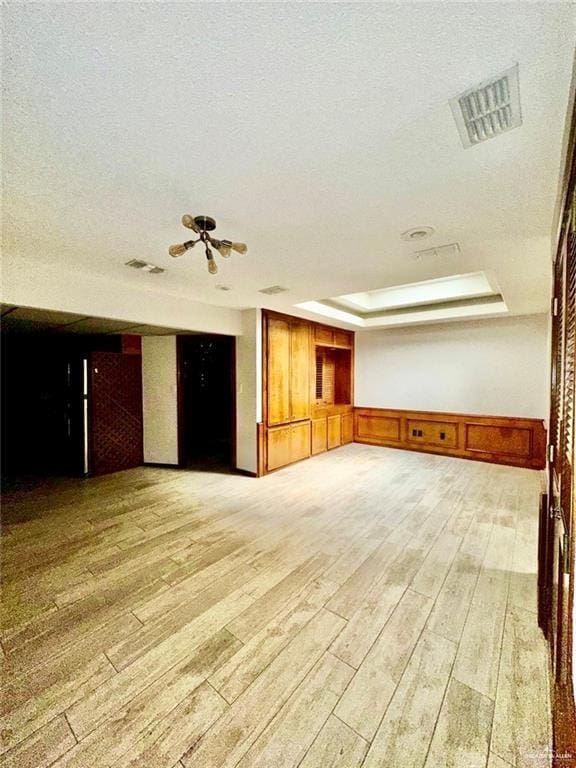 empty room featuring a raised ceiling, a textured ceiling, and light hardwood / wood-style flooring