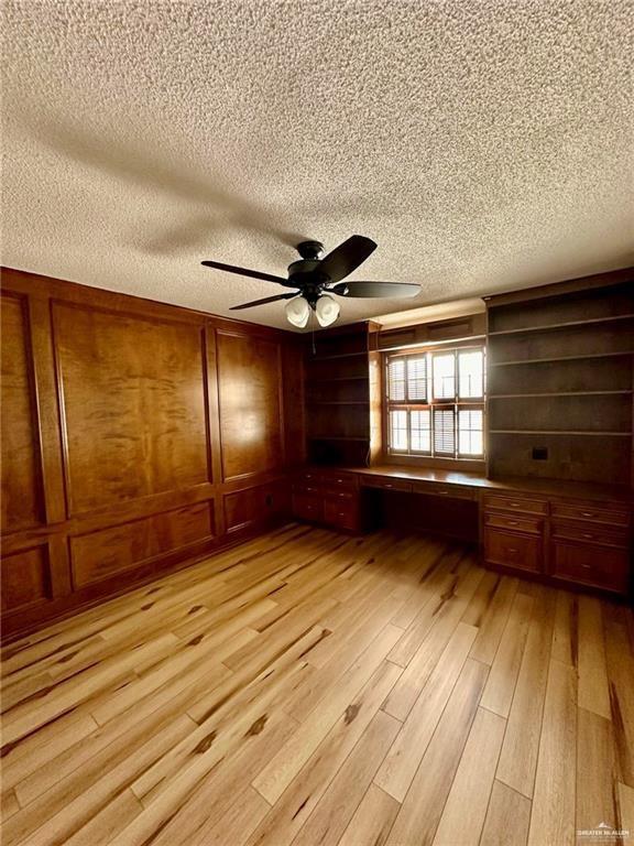 interior space featuring wood walls, ceiling fan, light hardwood / wood-style floors, and a textured ceiling