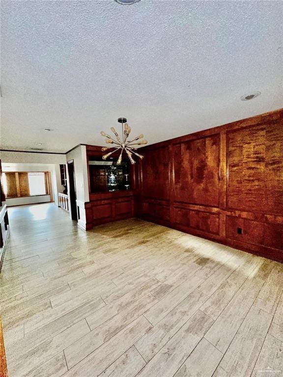 empty room featuring a chandelier, wooden walls, light hardwood / wood-style floors, and a textured ceiling