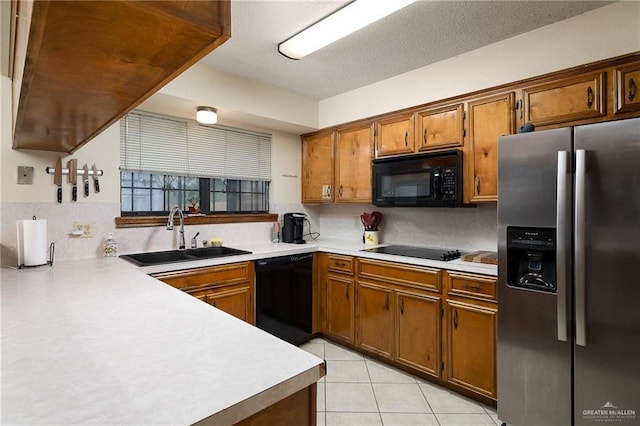 kitchen with light tile patterned floors, a sink, light countertops, brown cabinets, and black appliances