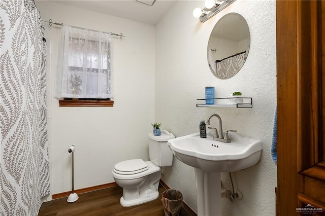 full bathroom featuring a textured wall, curtained shower, toilet, wood finished floors, and baseboards