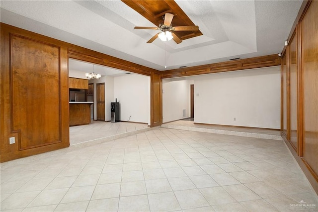 empty room featuring a tray ceiling, light tile patterned floors, a textured ceiling, baseboards, and ceiling fan with notable chandelier