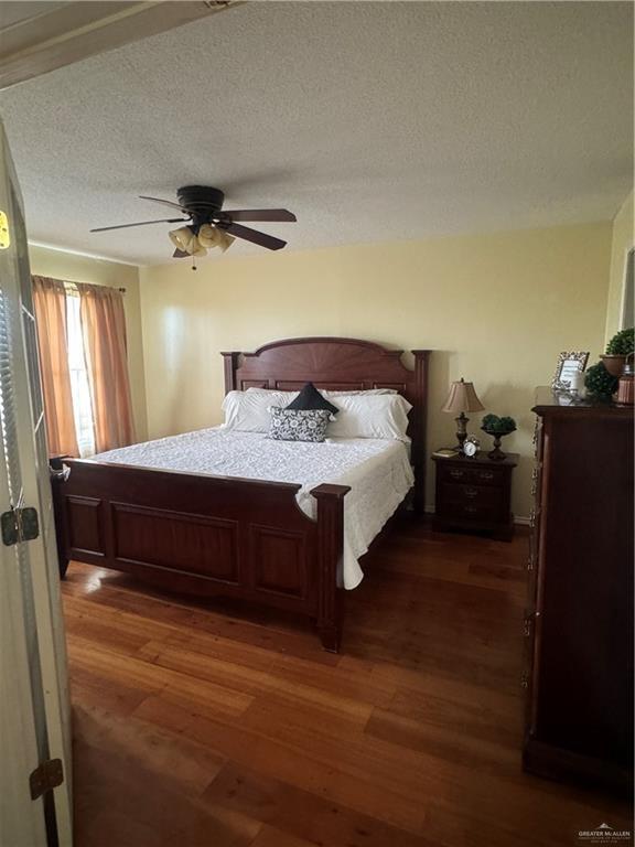 bedroom with ceiling fan, dark wood-type flooring, and a textured ceiling