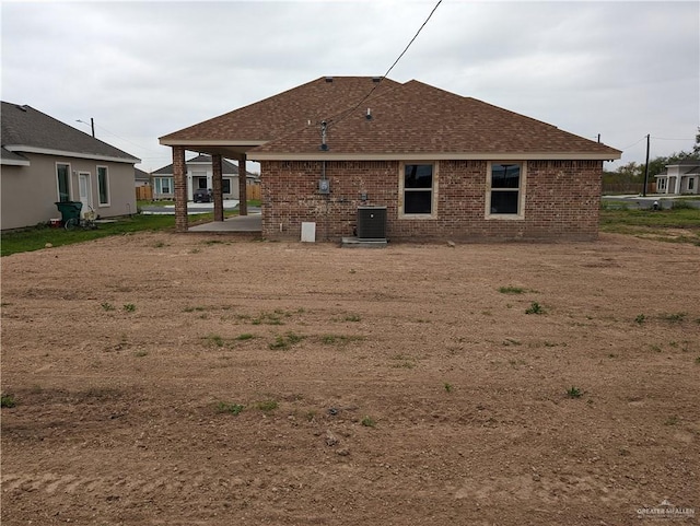 rear view of house with central AC unit, brick siding, roof with shingles, and a patio area