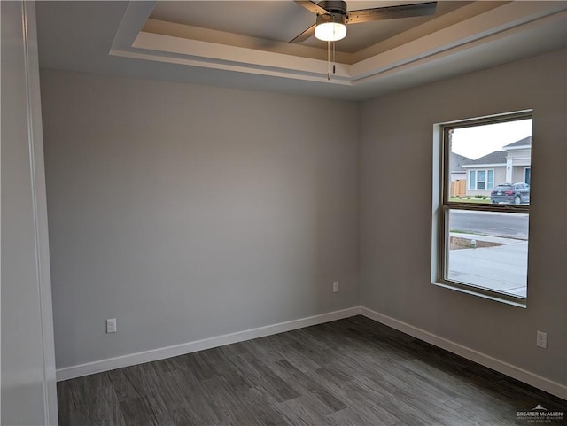 spare room featuring dark wood-style flooring, a raised ceiling, a ceiling fan, and baseboards