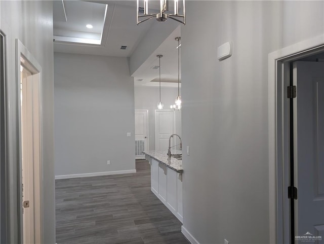 corridor featuring dark wood finished floors, a notable chandelier, visible vents, a sink, and baseboards