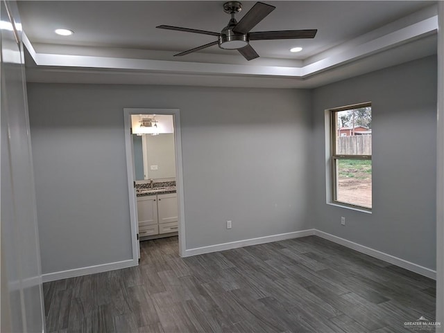 empty room with recessed lighting, a ceiling fan, baseboards, dark wood-style floors, and a tray ceiling