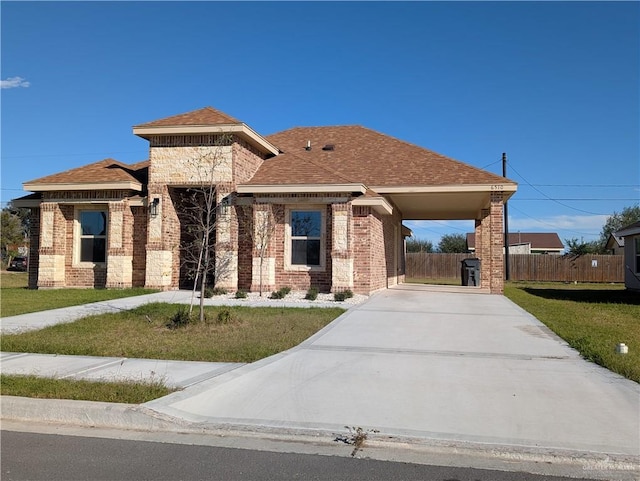 view of front facade featuring brick siding, a shingled roof, a front yard, fence, and driveway