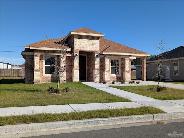 view of front facade featuring a shingled roof, a front lawn, and brick siding