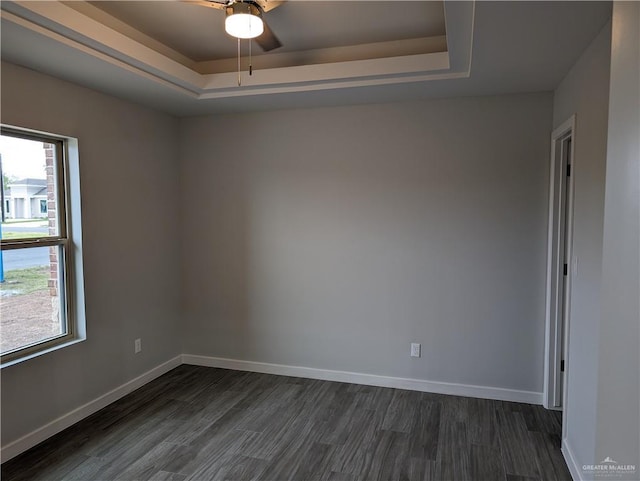 empty room with a tray ceiling, dark wood finished floors, baseboards, and ceiling fan