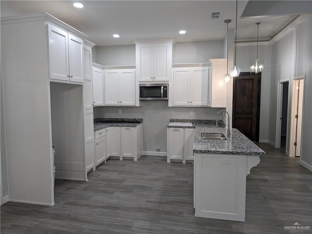 kitchen featuring visible vents, stainless steel microwave, hanging light fixtures, white cabinetry, and a sink