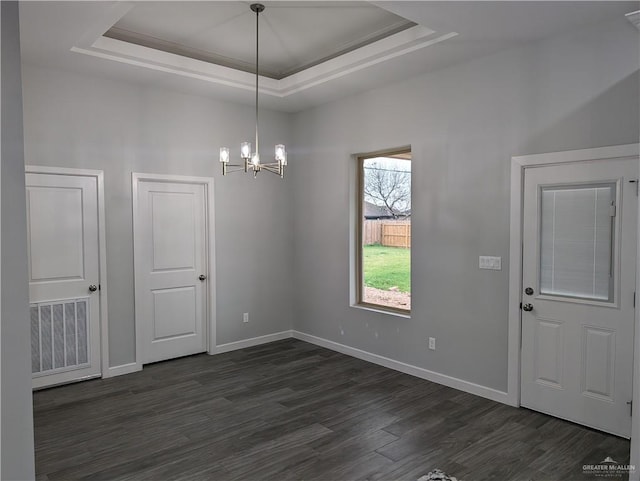 unfurnished dining area with a tray ceiling, dark wood finished floors, visible vents, an inviting chandelier, and baseboards