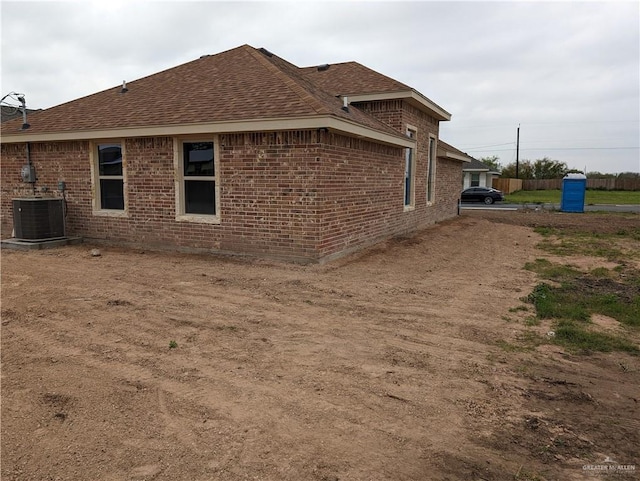 view of home's exterior featuring roof with shingles, central AC unit, and brick siding