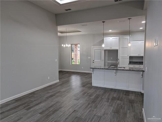 kitchen featuring white cabinets, a raised ceiling, dark wood-style floors, dark stone countertops, and a sink